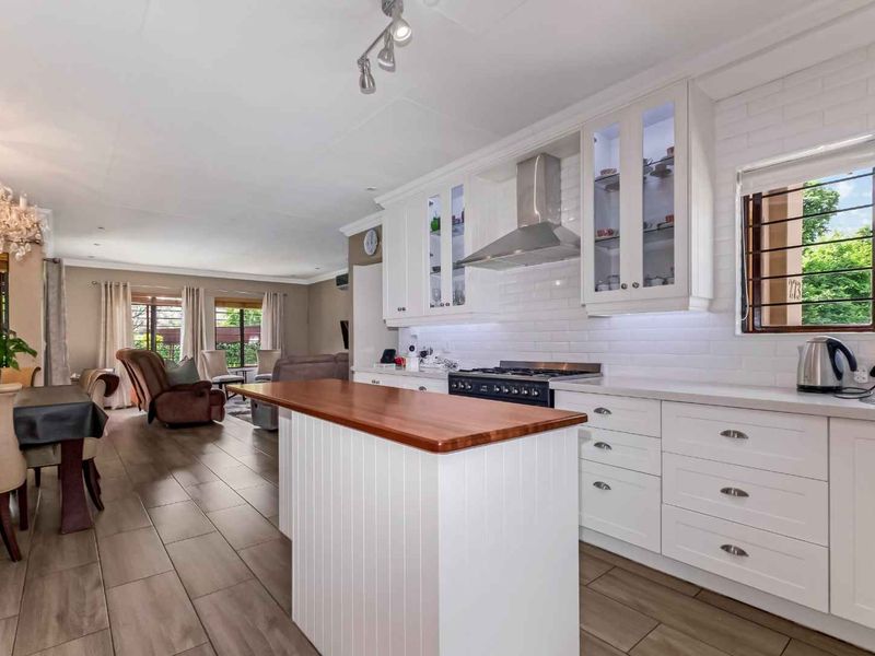 Spacious open-plan kitchen and living area featuring a central island with a wooden countertop, white cabinetry, and modern tiled flooring.