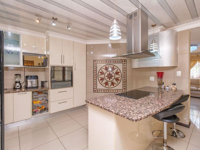 Modern kitchen featuring granite countertops, built-in oven, electric hob, stainless steel extractor fan, and decorative wall mosaic with tiled flooring.