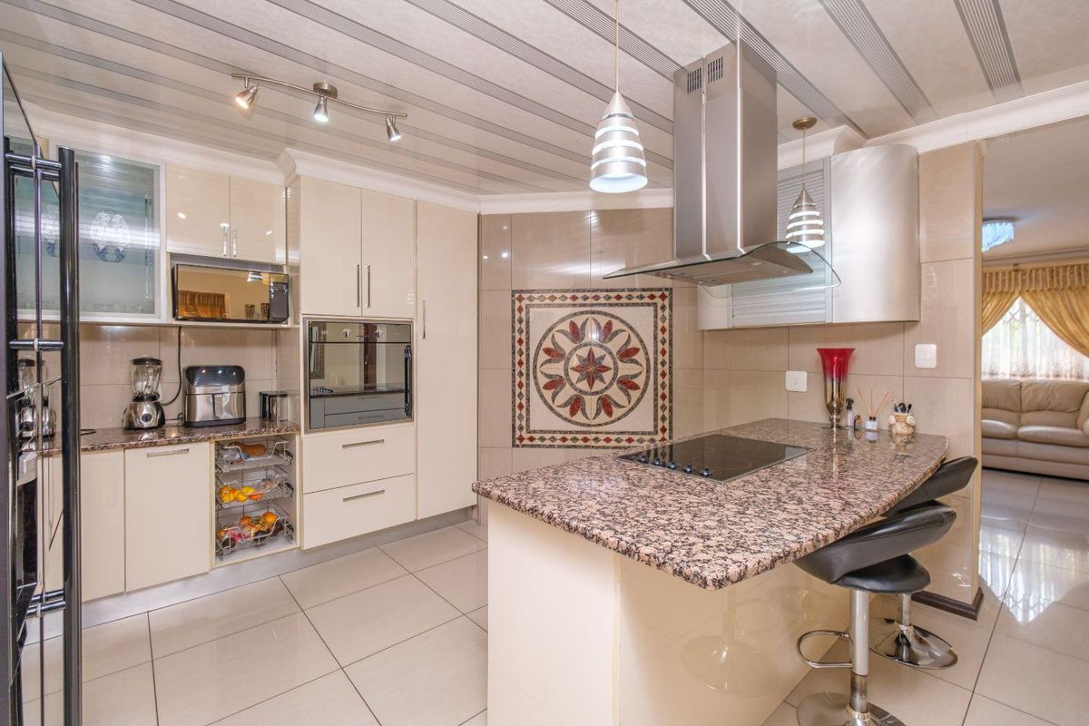 Modern kitchen featuring granite countertops, built-in oven, electric hob, stainless steel extractor fan, and decorative wall mosaic with tiled flooring.