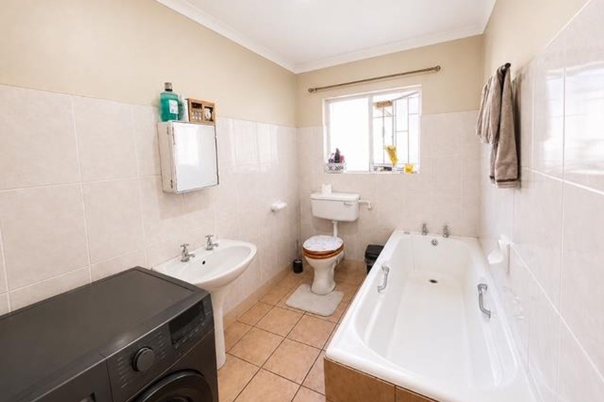 A functional bathroom featuring a pedestal basin, toilet, and bathtub with tiled walls and flooring, offering a clean and practical layout.