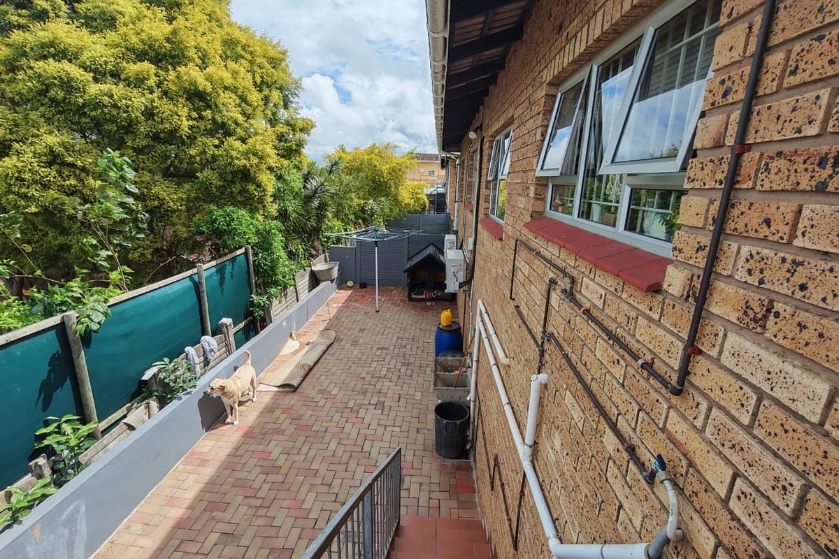 A rear exterior view of the townhouse featuring a paved patio area, face brick facade, and external plumbing infrastructure.