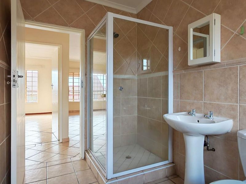 A functional bathroom featuring a pedestal basin, shower enclosure, and tiled finishes, presenting a clean and well-maintained space ready for potential cosmetic updates.
