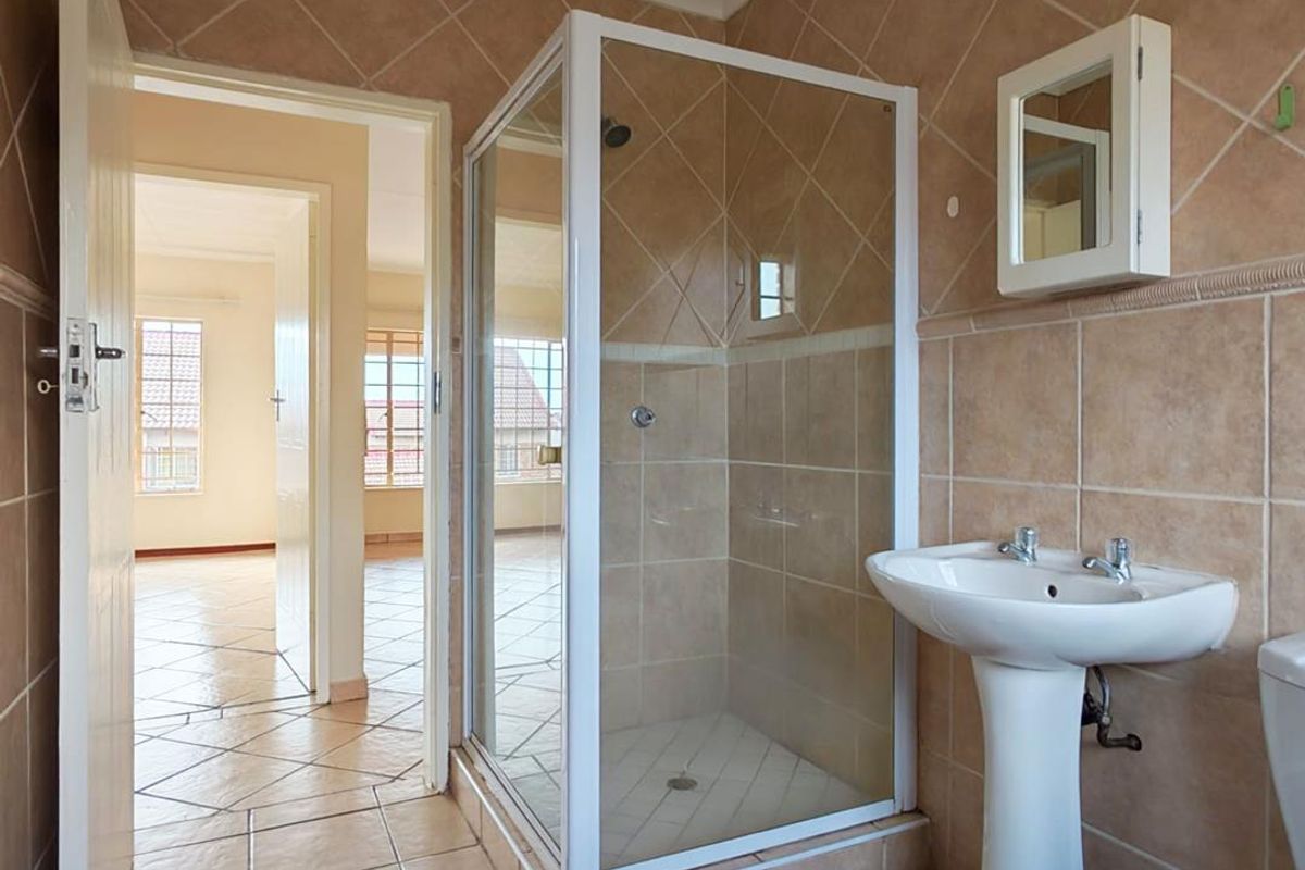 A functional bathroom featuring a pedestal basin, shower enclosure, and tiled finishes, presenting a clean and well-maintained space ready for potential cosmetic updates.