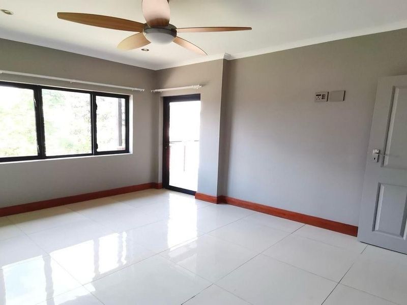 A bright, empty bedroom featuring neutral grey walls, white tiled flooring, a modern ceiling fan, and access to an outdoor area.