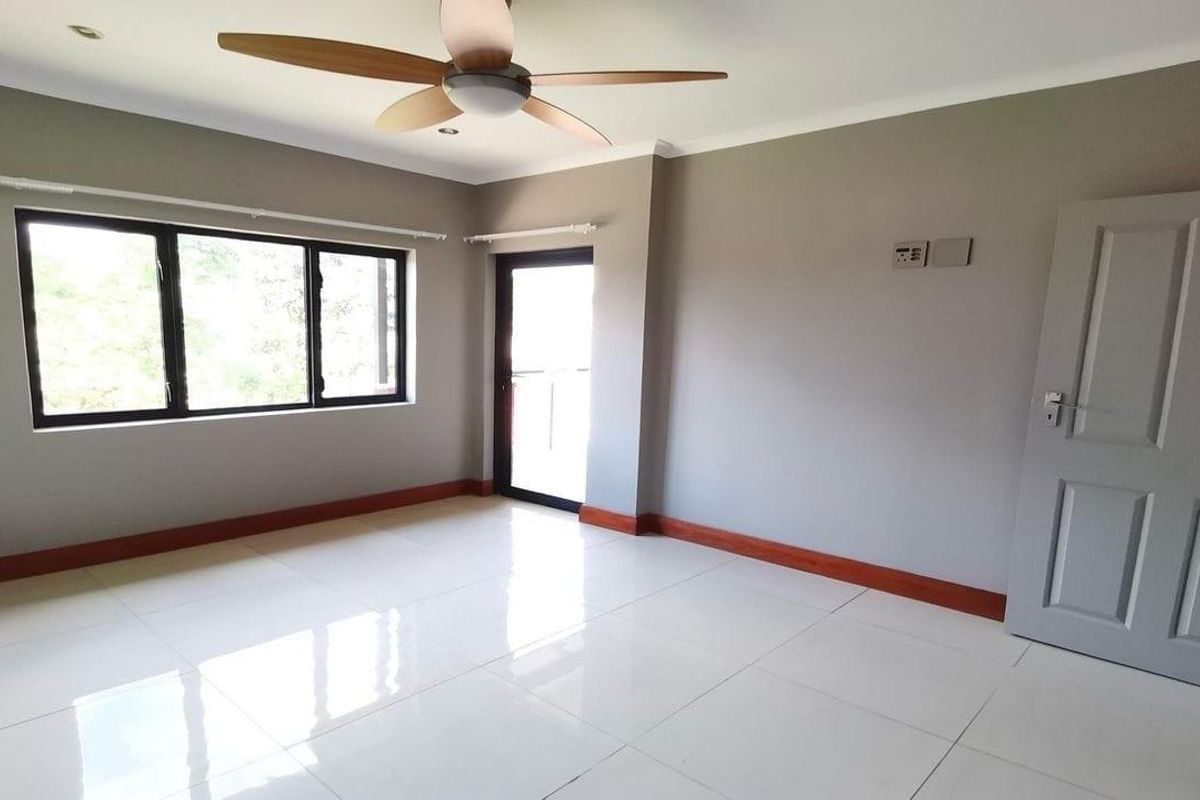 A bright, empty bedroom featuring neutral grey walls, white tiled flooring, a modern ceiling fan, and access to an outdoor area.