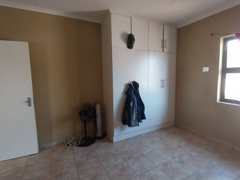 A bedroom featuring built-in cupboards, tiled flooring, and a window allowing natural light.