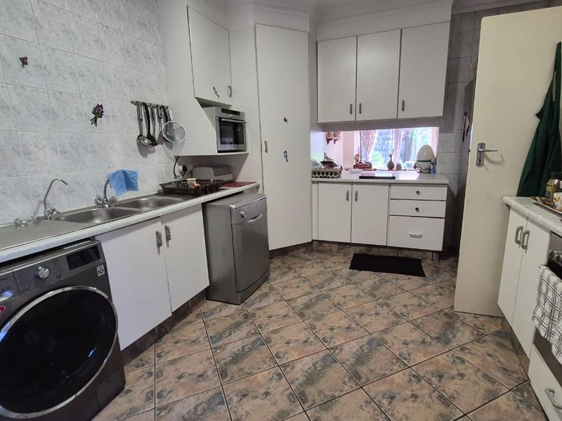 Functional kitchen featuring built-in cabinetry, double basin sink, integrated oven, and microwave with tiled backsplash and flooring.