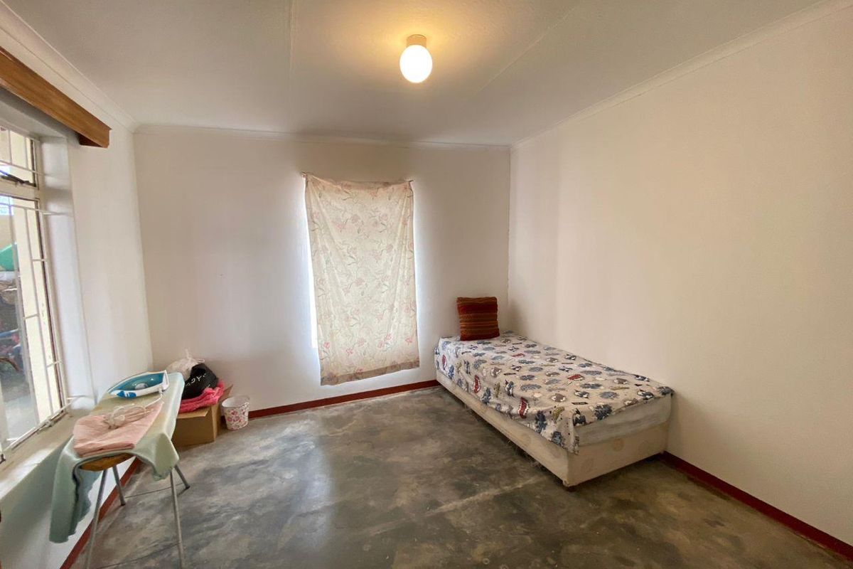 A simple bedroom featuring plain white walls, a single window, and exposed concrete flooring, offering a blank canvas for renovation.