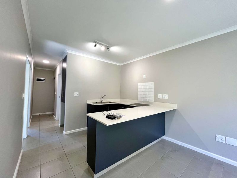 Modern kitchen featuring dark cabinetry, stone countertops, a built-in hob, and a subway tile splashback, set against neutral grey walls and tiled flooring.