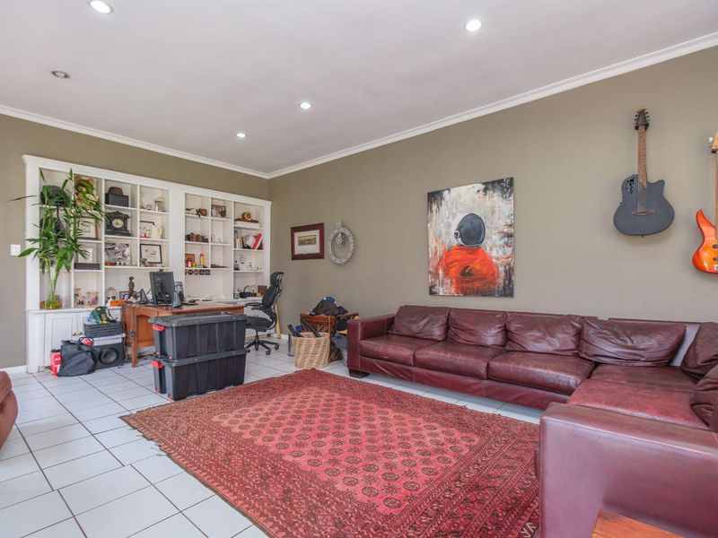 Spacious living room featuring tiled flooring, recessed downlighting, crown molding, and a large built-in shelving unit for storage or display.