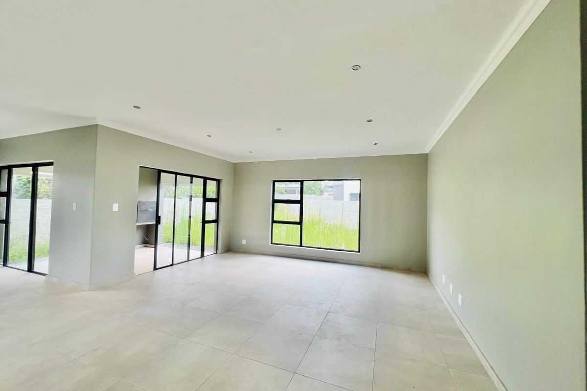 Spacious, light-filled living area featuring neutral tiled flooring, modern black aluminium window frames, and direct access to an outdoor patio space.