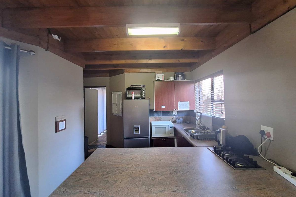 Functional kitchen featuring exposed timber beam ceilings, laminate countertops, a built-in gas hob, and fitted cabinetry with a view through to the hallway.