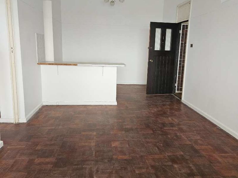 An empty open-plan living area featuring traditional parquet flooring and a built-in breakfast bar, offering a blank canvas for renovation.