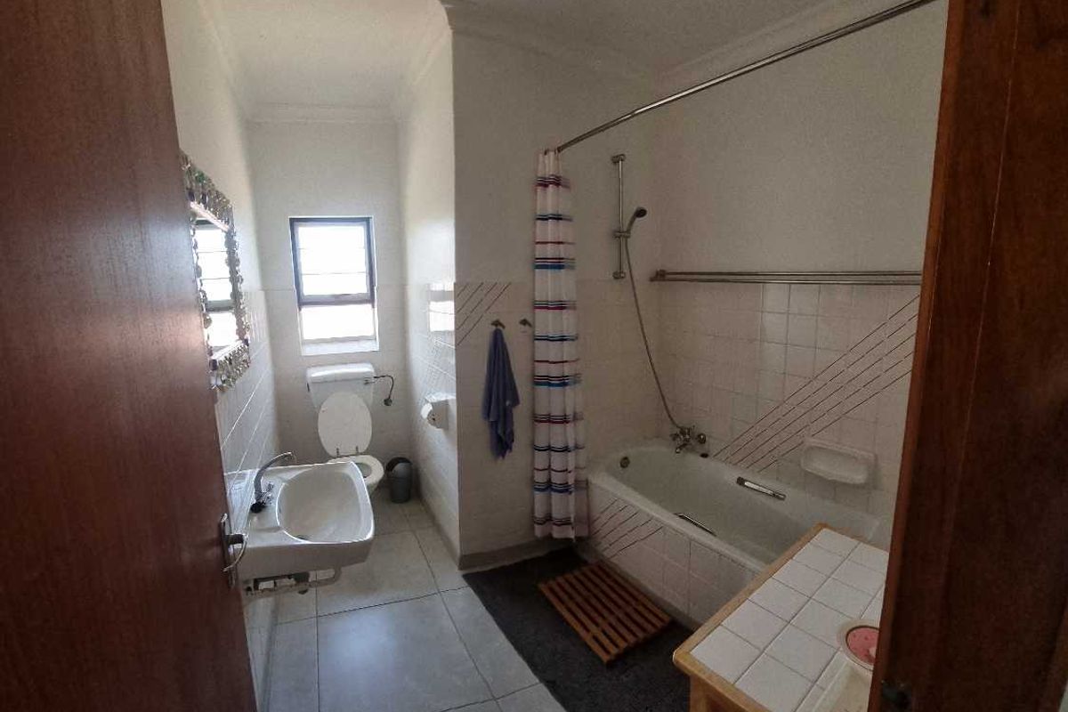 A functional bathroom featuring a bathtub with shower attachment, wall-mounted basin, and toilet, finished with neutral floor and wall tiling.