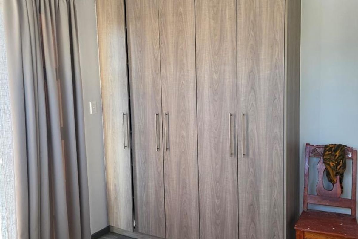 A bedroom featuring a modern, full-height built-in wardrobe with wood-grain finish and durable laminate flooring.