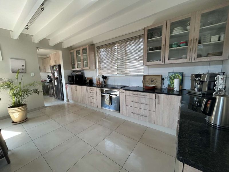 A well-maintained kitchen featuring light wood-grain cabinetry, dark granite countertops, built-in oven and hob, and exposed ceiling beams with tiled flooring.