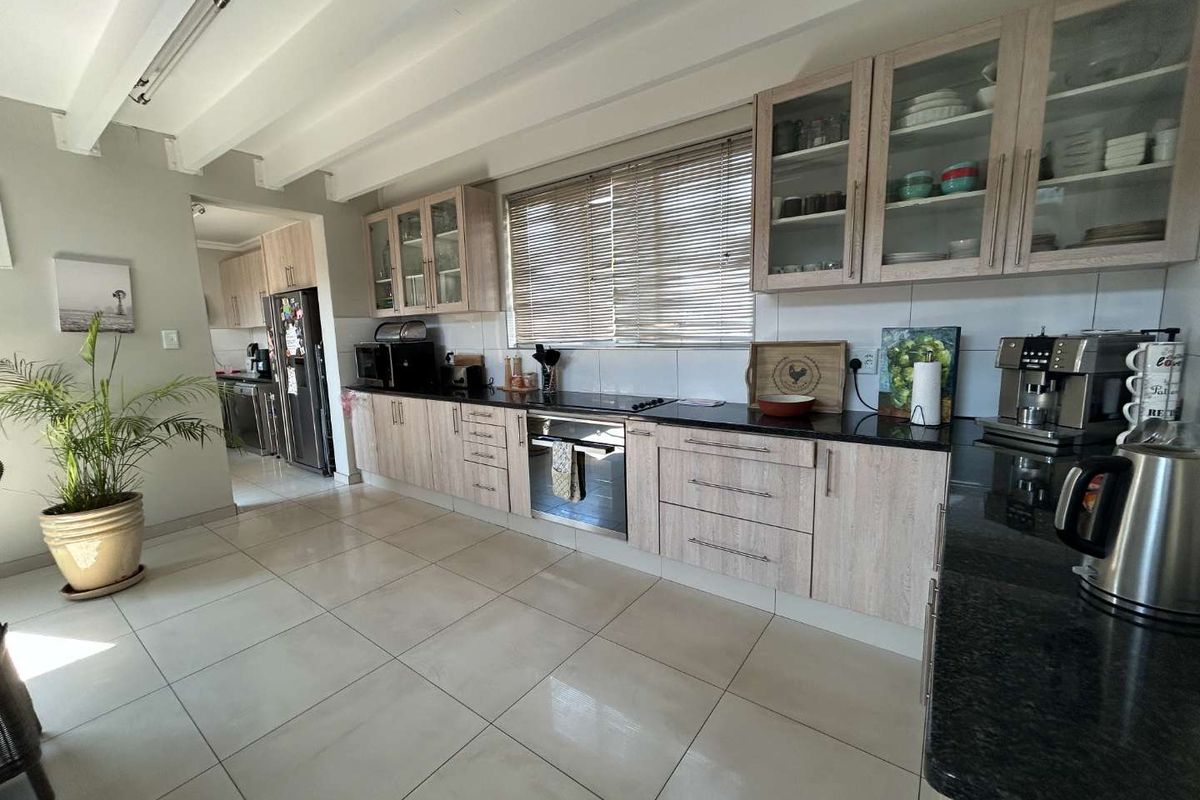 A well-maintained kitchen featuring light wood-grain cabinetry, dark granite countertops, built-in oven and hob, and exposed ceiling beams with tiled flooring.