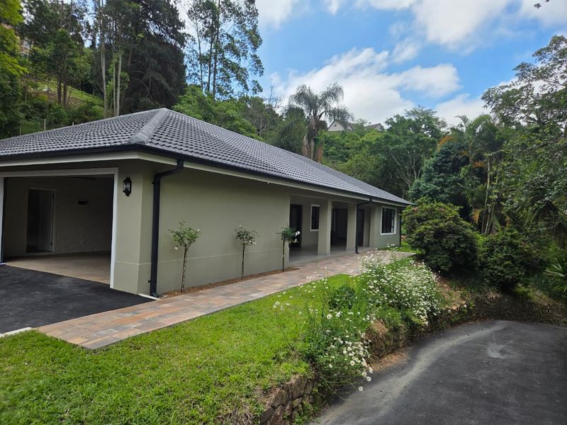 A well-maintained single-story home exterior featuring a tiled roof, integrated garage, and a paved walkway set within a lush, landscaped garden environment.