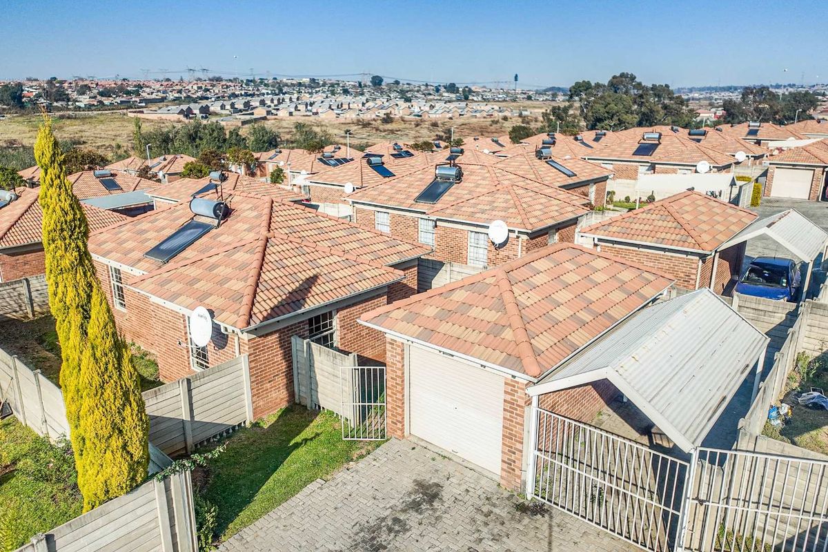 Aerial view of a residential estate featuring brick houses with tiled roofs, solar geysers, paved driveways, and perimeter walling.