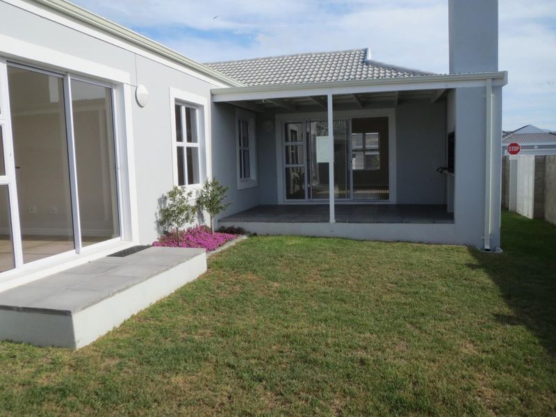 A well-maintained rear exterior view featuring a covered patio with tiled flooring, a built-in fireplace, and access to the garden via sliding glass doors.
