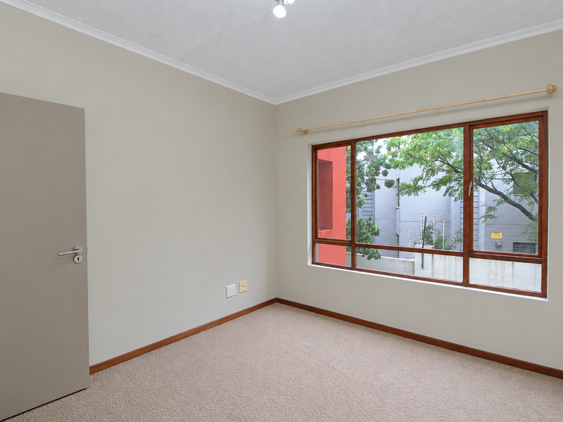 A clean, empty bedroom featuring neutral wall tones, carpeted flooring, and large timber-framed windows providing natural light and a view of the exterior.