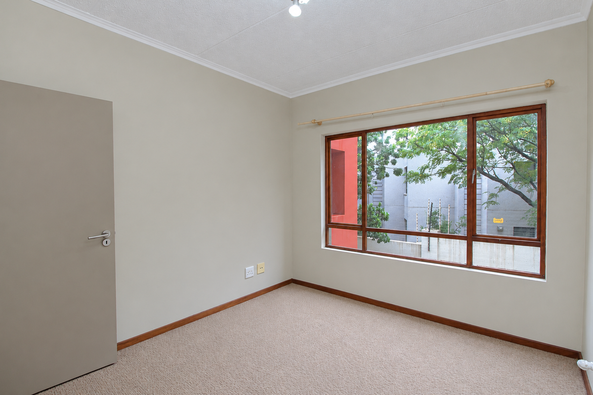A clean, empty bedroom featuring neutral wall tones, carpeted flooring, and large timber-framed windows providing natural light and a view of the exterior.