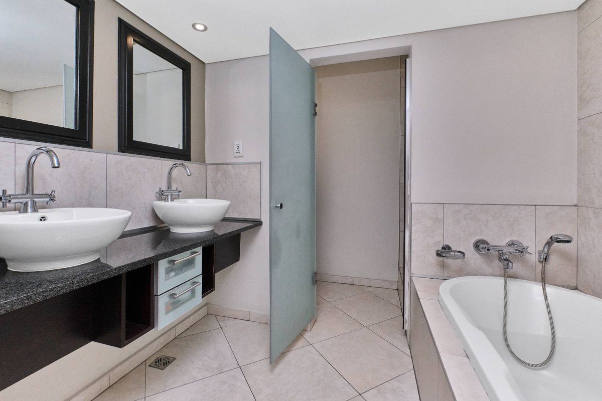 Modern bathroom featuring a double vanity with vessel sinks, granite countertop, tiled flooring, a built-in bathtub with shower mixer, and a frosted glass door.