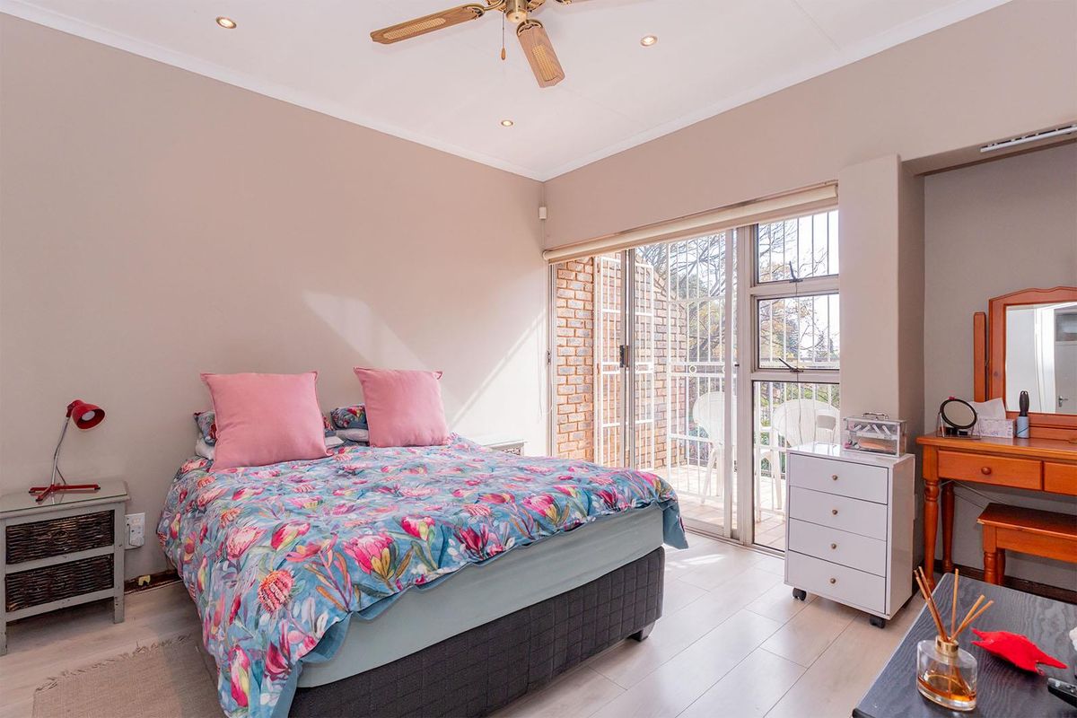 A bright bedroom featuring light-toned laminate flooring, a ceiling fan, and large sliding glass doors that open onto a private balcony.