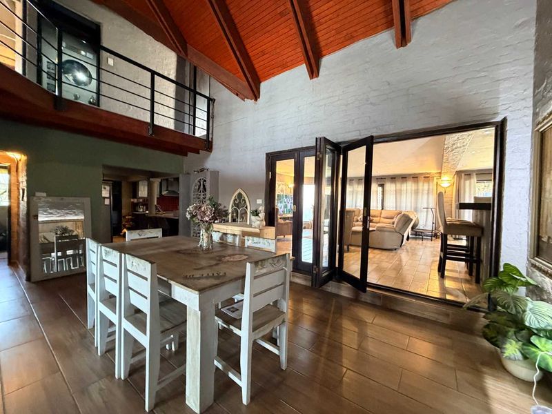 Spacious open-plan living area featuring high vaulted ceilings with exposed timber rafters, a mezzanine level, and bi-fold doors leading to an adjacent room.