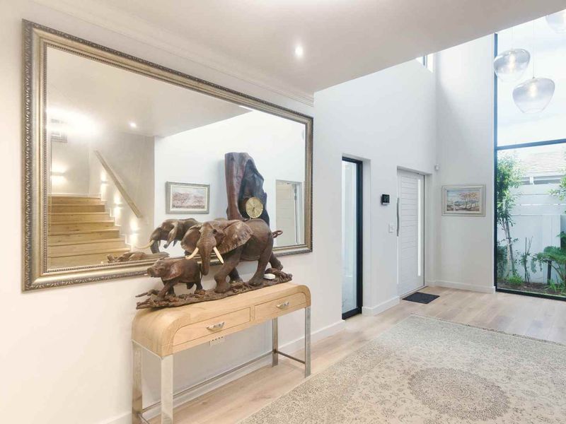 Bright and spacious double-volume entrance hall featuring modern timber flooring, a feature staircase, and large floor-to-ceiling windows overlooking a private courtyard.