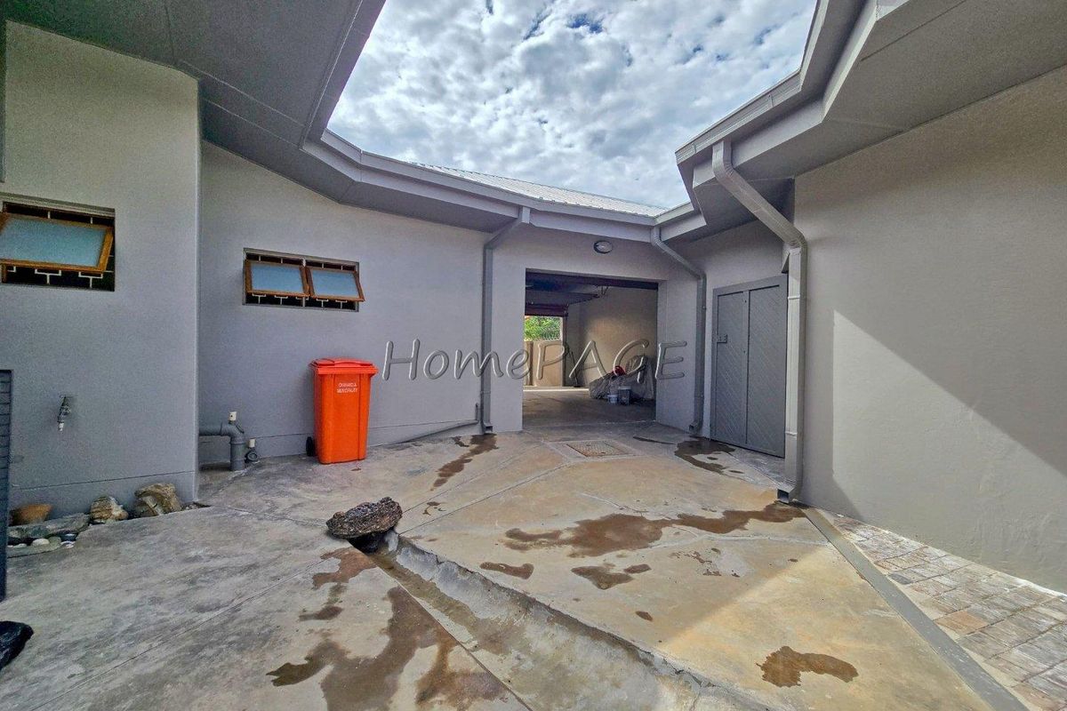 An open-air courtyard or utility area featuring concrete flooring, drainage systems, and access to adjacent building sections.
