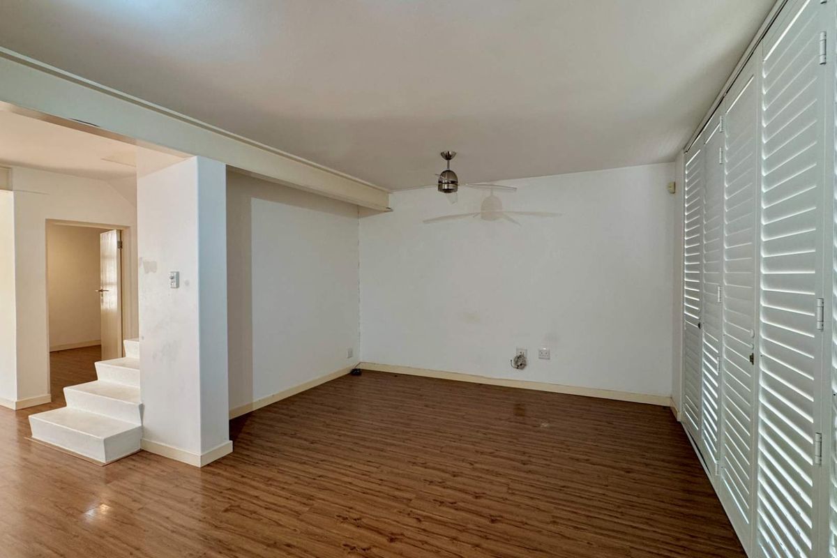 Spacious, empty living area featuring laminate flooring, a ceiling fan, and white plantation-style shutters, with an adjacent staircase leading to another level.