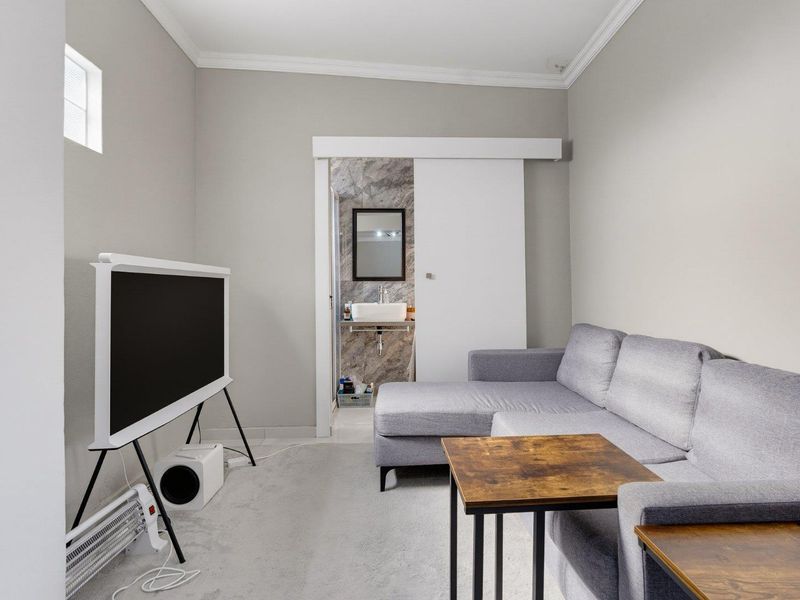 A compact living room featuring neutral walls, crown molding, and a sliding door providing access to an adjoining bathroom.