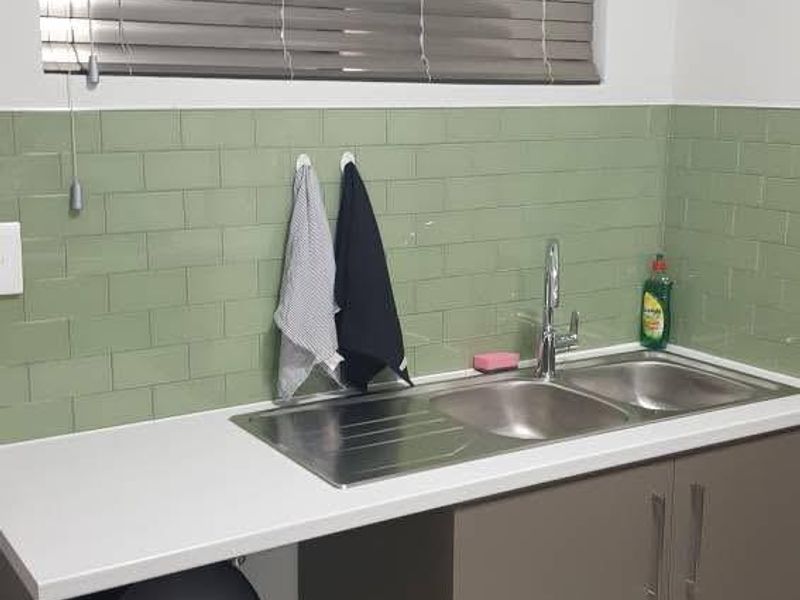 A functional kitchen area featuring a double bowl stainless steel sink, modern subway tile splashback, and neutral cabinetry with integrated storage.