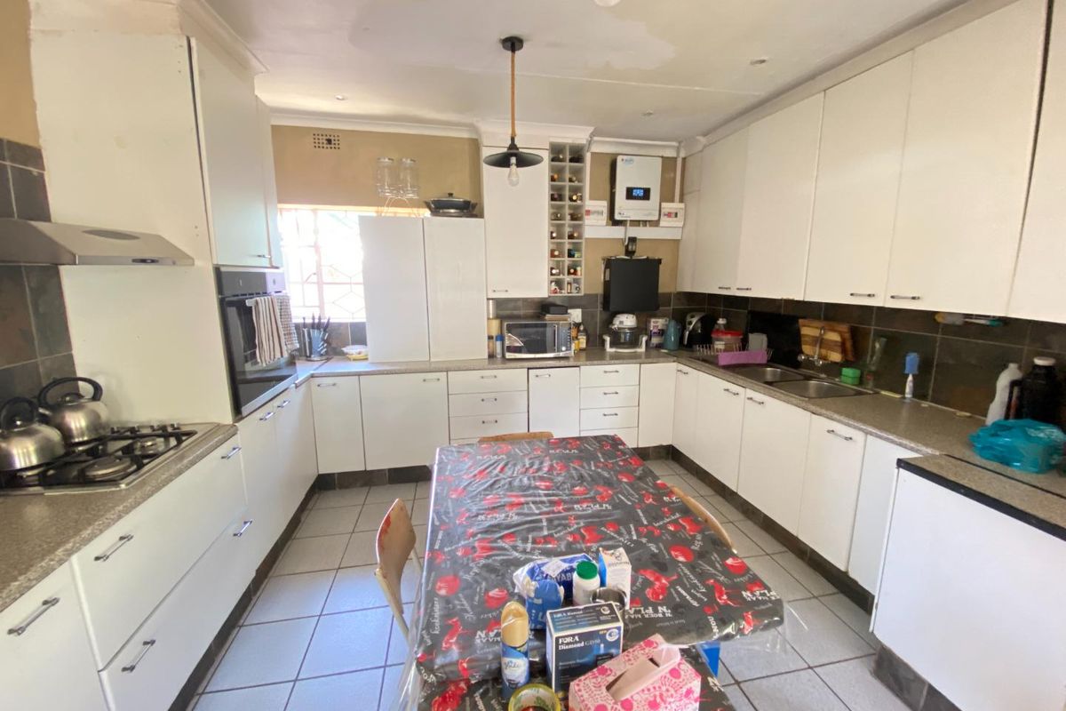 A functional kitchen featuring white cabinetry, built-in oven, gas hob, extractor fan, and double basin sink with tiled flooring.