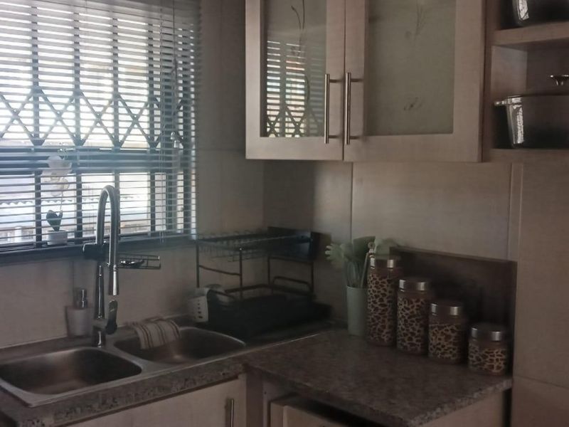 A functional kitchen area featuring a double bowl stainless steel sink, gooseneck mixer tap, laminate countertops, and ample upper cabinetry with glass-fronted doors.