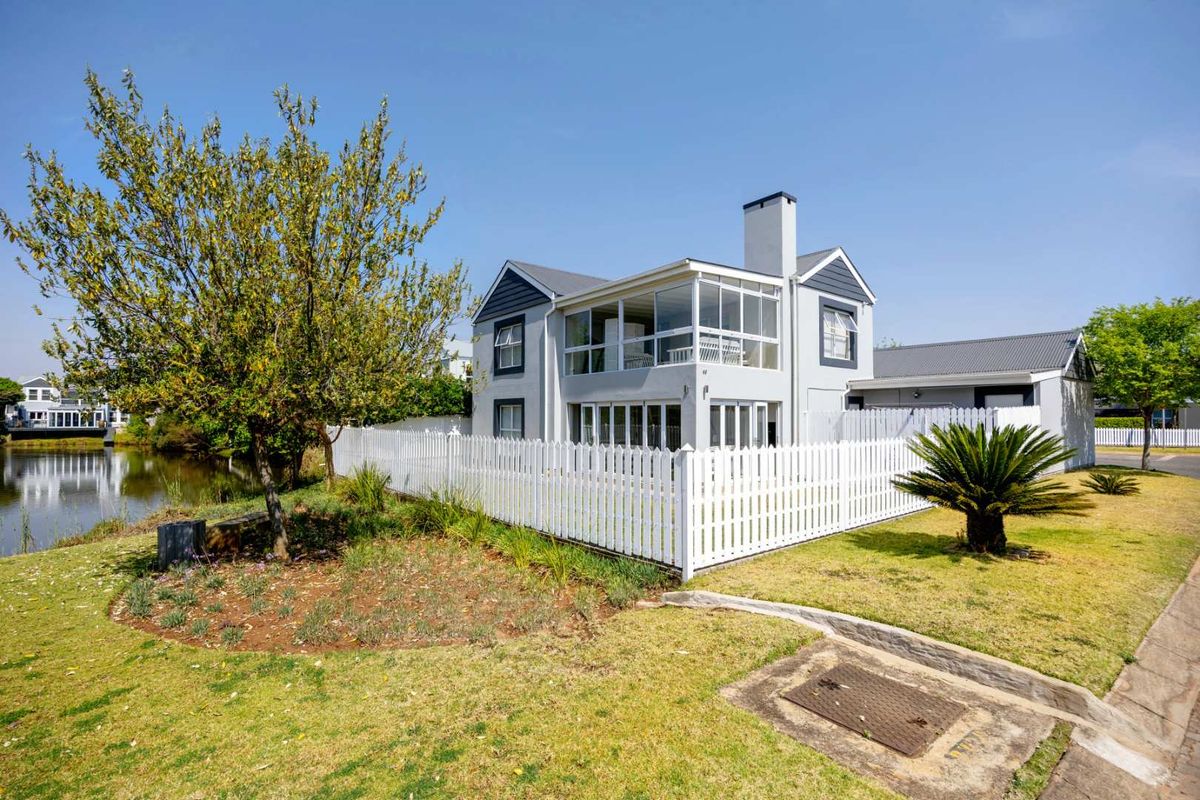 A well-maintained two-story house featuring a white picket fence, an enclosed upper balcony, and a chimney, situated near a waterfront area.
