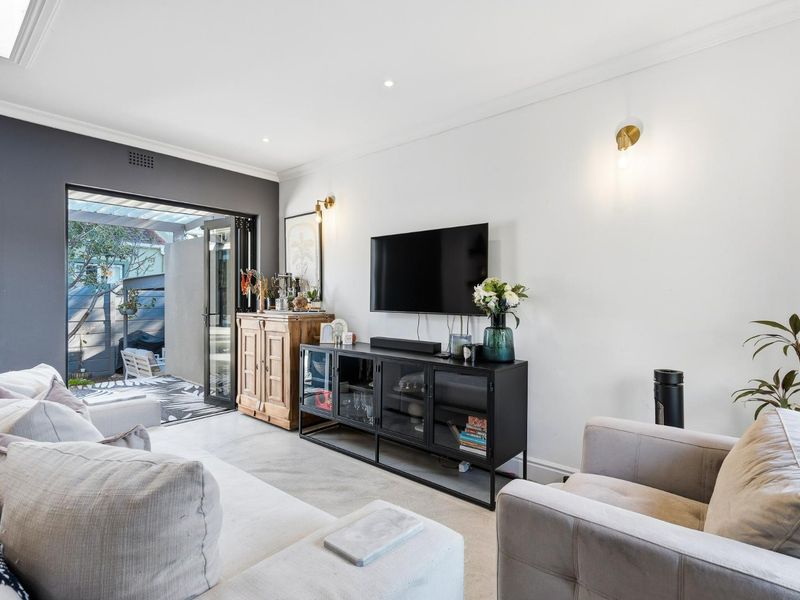 A bright living room featuring modern downlights, elegant cornicing, and bi-fold doors that provide seamless access to the outdoor patio area.