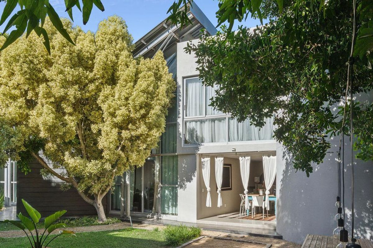 A view of the rear exterior of the modern home, featuring large glass windows, a covered patio area, and a landscaped garden.