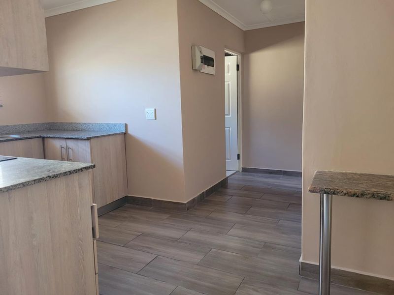 A clean, modern kitchen area featuring light wood-look cabinetry, granite countertops, and durable tiled flooring with an integrated breakfast bar.