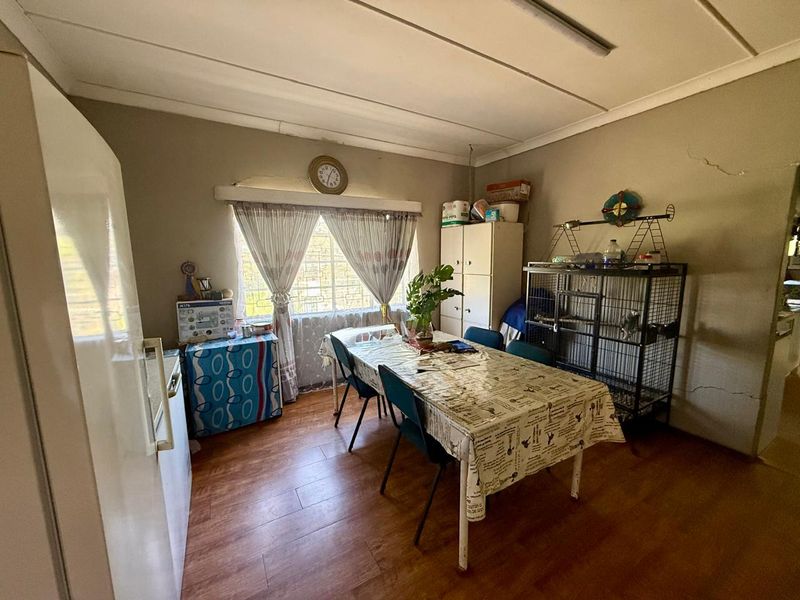 A dining area featuring laminate flooring, a window with security bars, and built-in storage, showing signs of wear including cracked wall plaster.