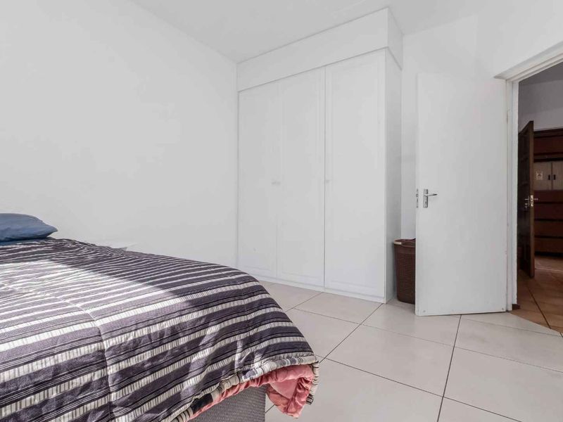 A bedroom featuring tiled flooring and a built-in wardrobe, with a doorway leading to an adjacent room.