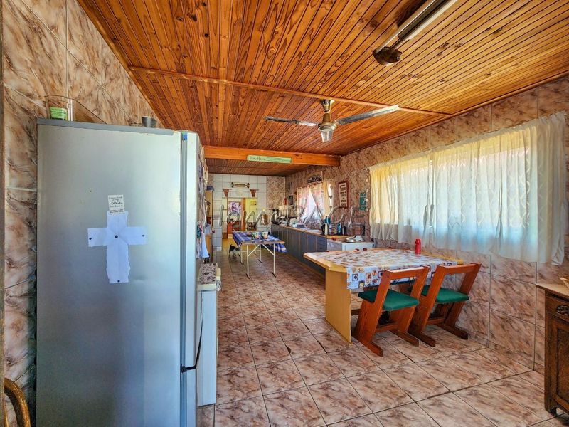 A spacious kitchen featuring tiled walls and flooring with a timber-clad ceiling, offering significant potential for a modern renovation.