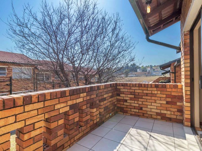 A private balcony featuring exposed brick walls, tiled flooring, and a covered roof section, offering an open outdoor space.