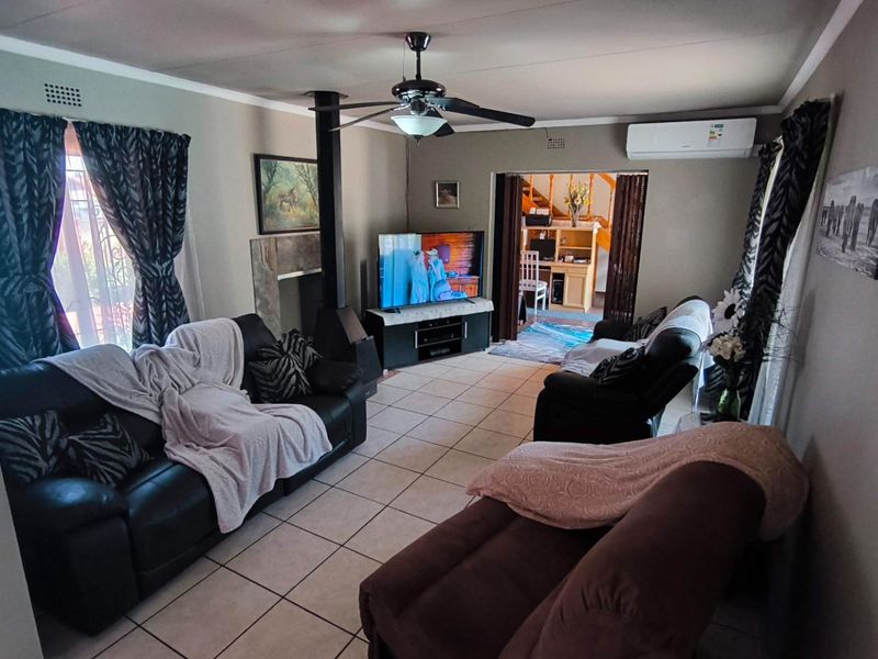 A comfortable living room featuring a freestanding fireplace, ceiling fan, and split-system air conditioning, finished with neutral floor tiles.