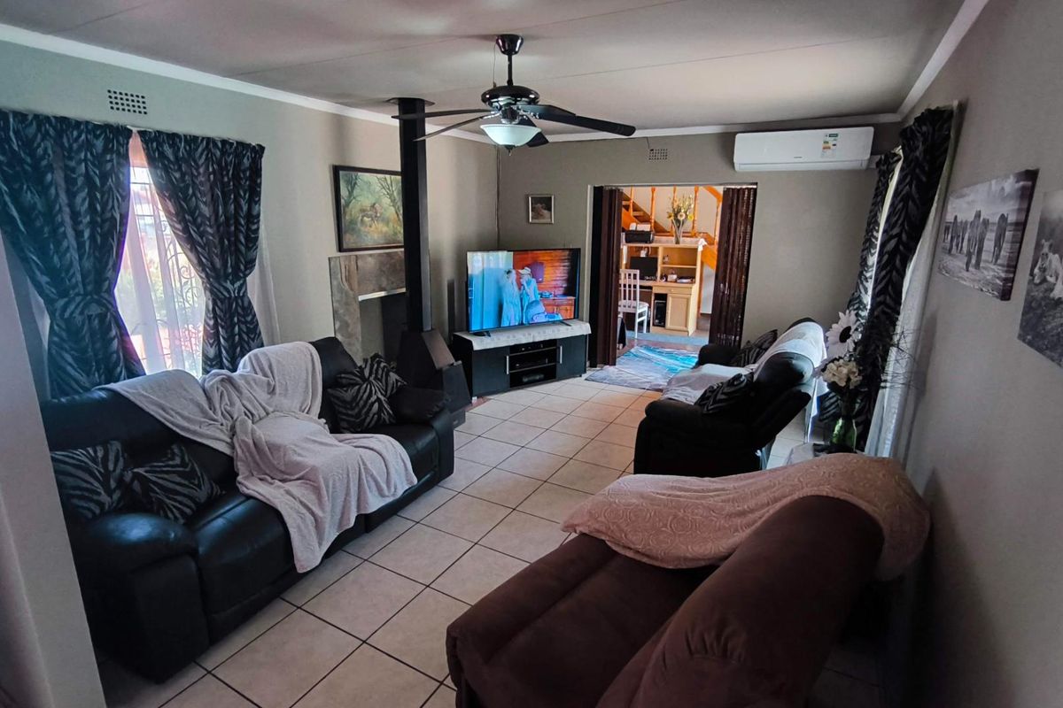 A comfortable living room featuring a freestanding fireplace, ceiling fan, and split-system air conditioning, finished with neutral floor tiles.