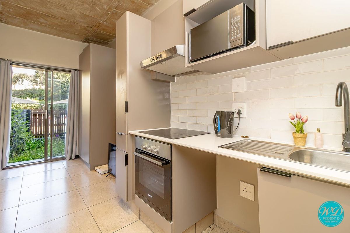 Modern kitchen featuring sleek cabinetry, built-in appliances, subway tile backsplash, and direct access to an outdoor patio area.