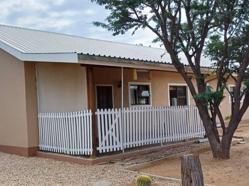A view of the rear exterior of the house featuring a covered patio area with a white picket fence and a corrugated metal roof.