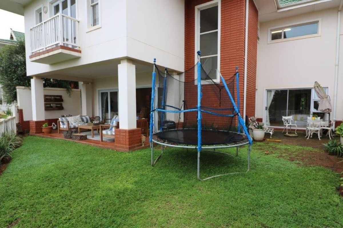 Rear view of the property featuring a covered patio area, a balcony, and a well-maintained garden space.