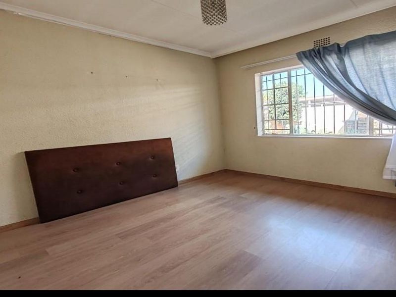 A spacious bedroom featuring light-toned laminate flooring, security bars on the window, and neutral wall finishes, offering a blank canvas for personalization.